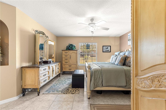 bedroom featuring baseboards, a textured ceiling, light tile patterned flooring, arched walkways, and a ceiling fan