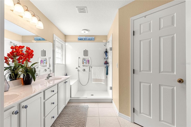 full bathroom featuring a stall shower, tile patterned flooring, a sink, and a textured ceiling