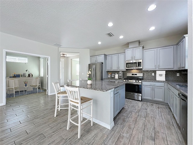 kitchen with dark stone countertops, a breakfast bar area, light wood finished floors, appliances with stainless steel finishes, and a kitchen island