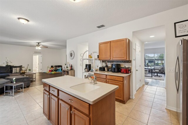kitchen with a sink, ceiling fan, visible vents, freestanding refrigerator, and a center island