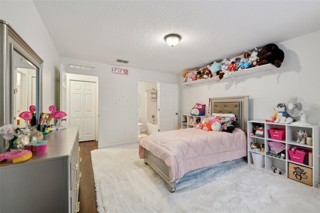 bedroom featuring visible vents, wood finished floors, ensuite bath, and a textured ceiling