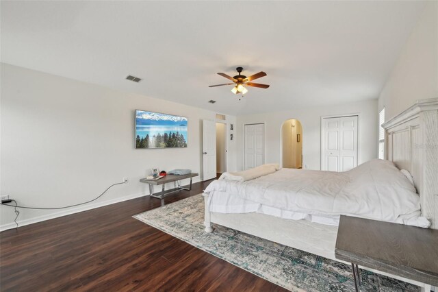 bedroom featuring visible vents, arched walkways, baseboards, wood finished floors, and multiple closets