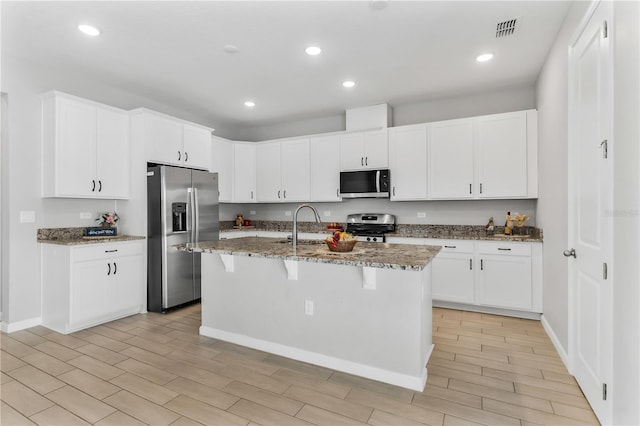 6003 Nightjar Ct, Okahumpka, FL 34762 - kitchen with an island with sink, a kitchen breakfast bar, appliances with stainless steel finishes, dark stone countertops, and white cabinets
