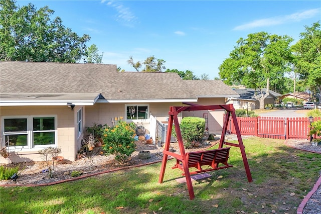 rear view of house featuring concrete block siding, a shingled roof, fence, and a yard