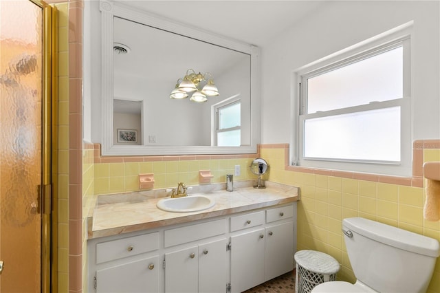 bathroom with vanity, tile walls, a shower stall, a wainscoted wall, and visible vents