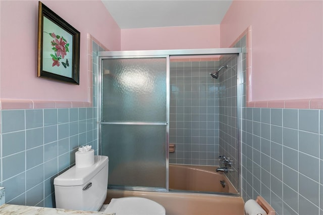 full bath featuring tile walls, wainscoting, toilet, and shower / bath combination with glass door