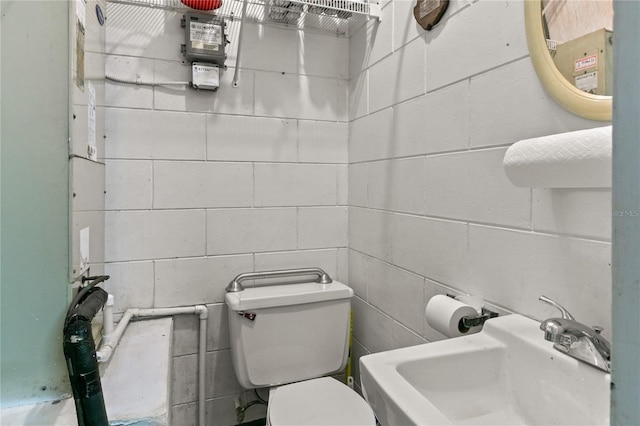 half bathroom featuring concrete block wall, a sink, and toilet