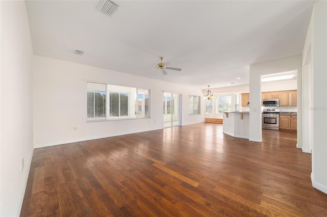 unfurnished living room featuring dark wood-style flooring, ceiling fan with notable chandelier, baseboards, and visible vents