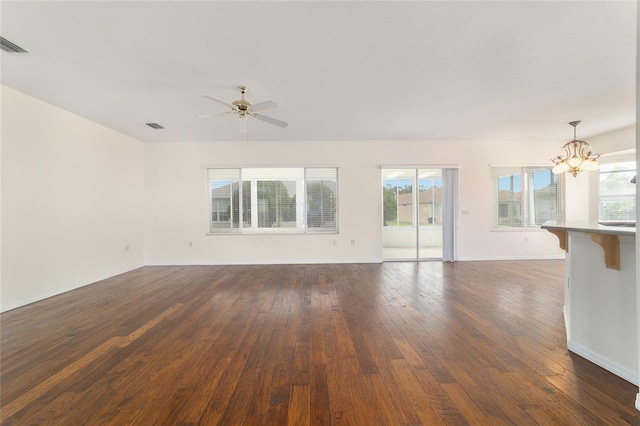 unfurnished living room featuring dark wood-style flooring, ceiling fan with notable chandelier, a healthy amount of sunlight, and visible vents