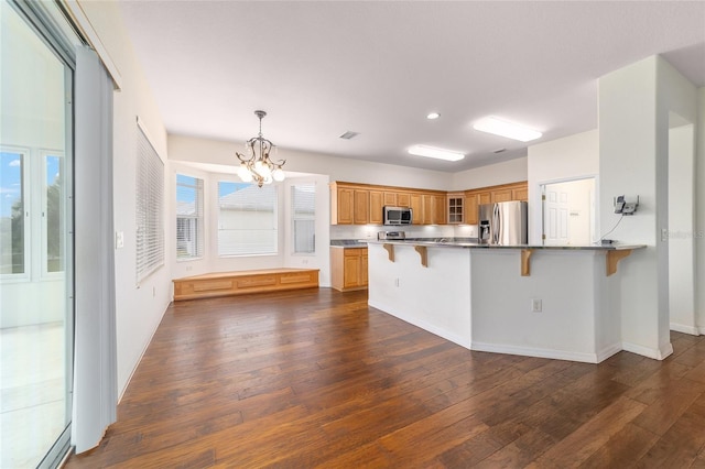 kitchen featuring dark wood-style flooring, a breakfast bar, appliances with stainless steel finishes, and a peninsula