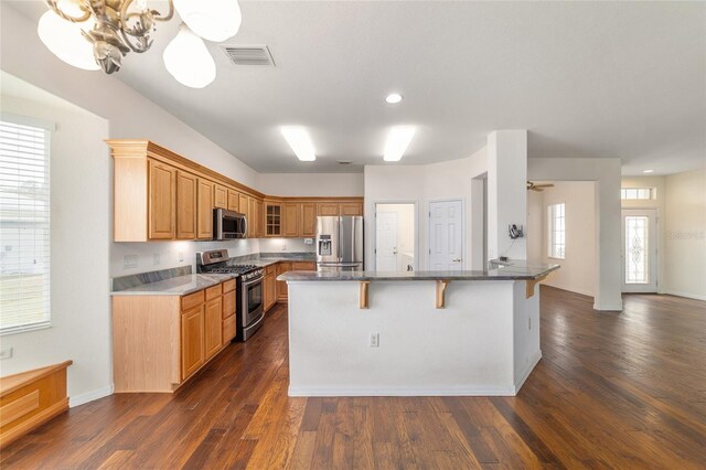 kitchen with visible vents, a breakfast bar, appliances with stainless steel finishes, glass insert cabinets, and dark wood-style floors