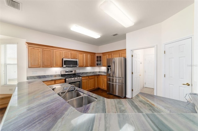 kitchen featuring visible vents, stainless steel appliances, glass insert cabinets, a sink, and brown cabinetry