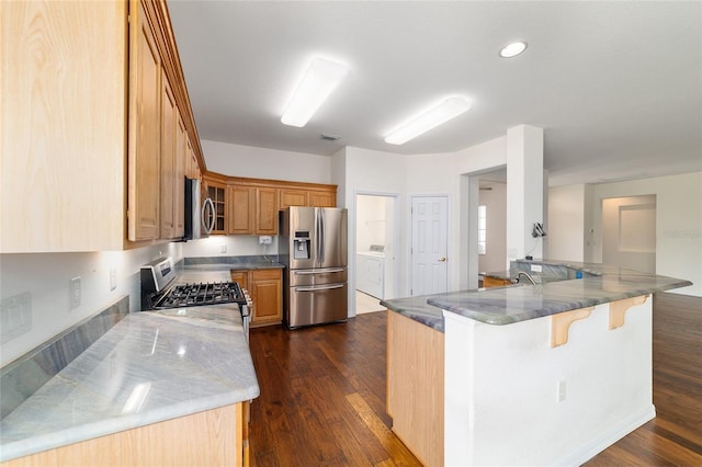kitchen featuring a kitchen bar, dark wood-style flooring, appliances with stainless steel finishes, and brown cabinets