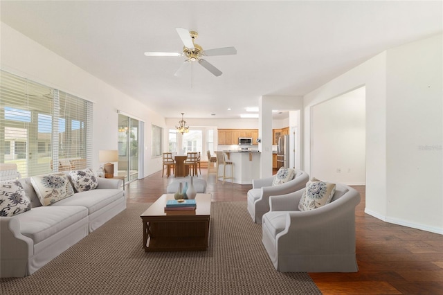 living room with baseboards, wood finished floors, and ceiling fan with notable chandelier