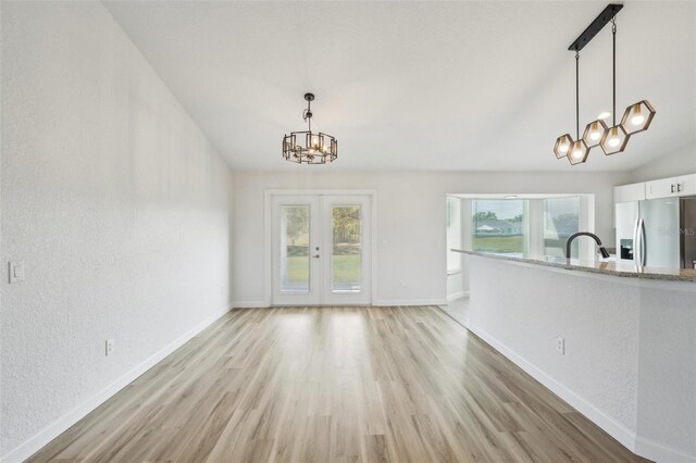 2575 SE 75th Blvd, Bushnell, FL 33513 - unfurnished dining area featuring french doors, light wood-style flooring, baseboards, vaulted ceiling, and a notable chandelier