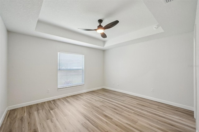 2575 SE 75th Blvd, Bushnell, FL 33513 - spare room featuring a tray ceiling, a ceiling fan, a textured ceiling, light wood-style flooring, and baseboards