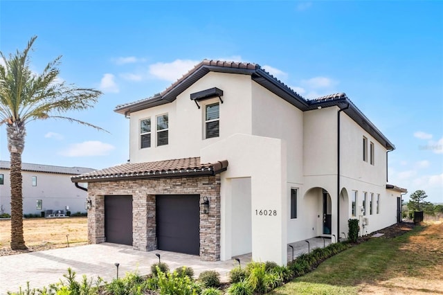 mediterranean / spanish house featuring stucco siding, stone siding, a tiled roof, driveway, and a garage