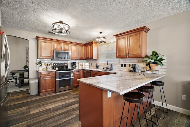 2142 Margarita Dr, The Villages, FL 32159 - kitchen featuring a notable chandelier, brown cabinetry, a peninsula, and stainless steel appliances