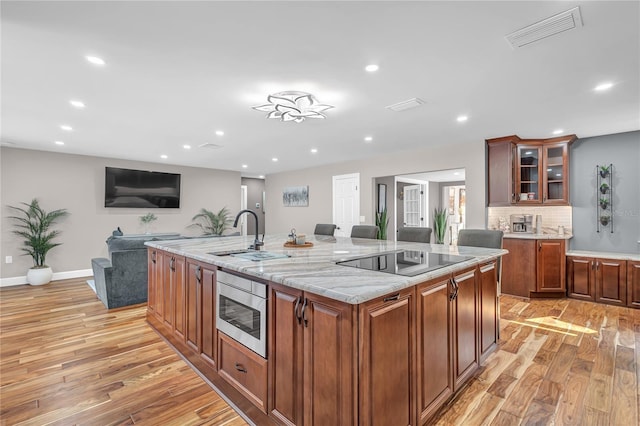 11619 Lane Park Rd, Tavares, FL 32778 - kitchen with stainless steel microwave, light wood finished floors, black electric cooktop, a large island with sink, and recessed lighting