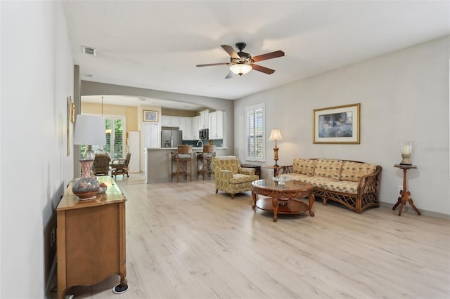 living room featuring light wood finished floors, visible vents, ceiling fan, and a healthy amount of sunlight