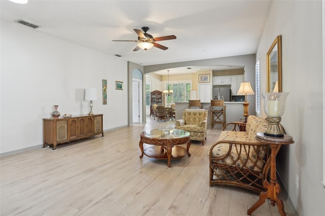 living area featuring light wood-style floors, baseboards, ceiling fan with notable chandelier, visible vents, and arched walkways