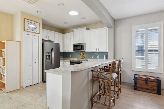 kitchen with white cabinets, light countertops, a peninsula, stainless steel appliances, and a breakfast bar area