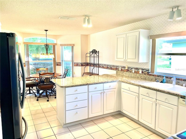 kitchen featuring white cabinets, a peninsula, wallpapered walls, a sink, and freestanding refrigerator
