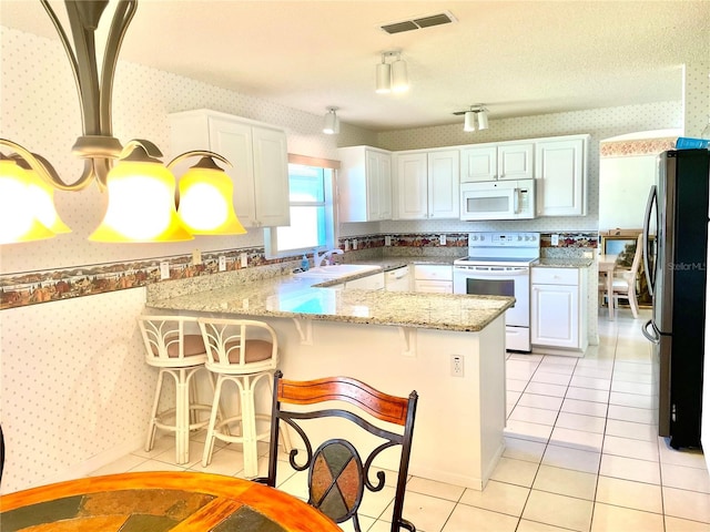 kitchen with wallpapered walls, visible vents, a peninsula, and white appliances