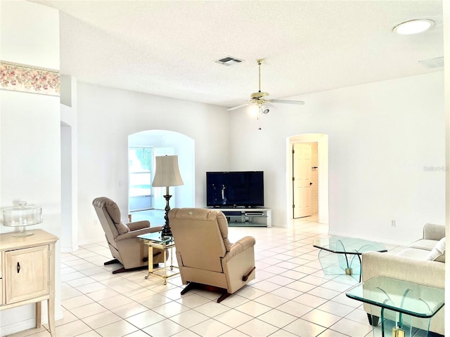 living room featuring light tile patterned floors, a textured ceiling, arched walkways, ceiling fan, and visible vents