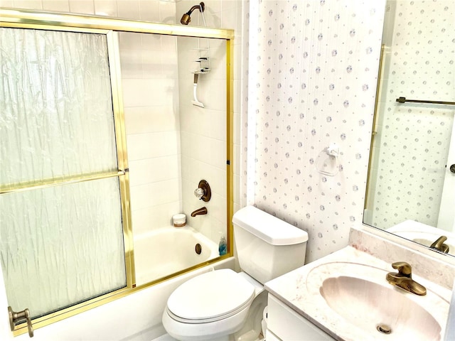 bathroom with combined bath / shower with glass door, vanity, toilet, and wallpapered walls