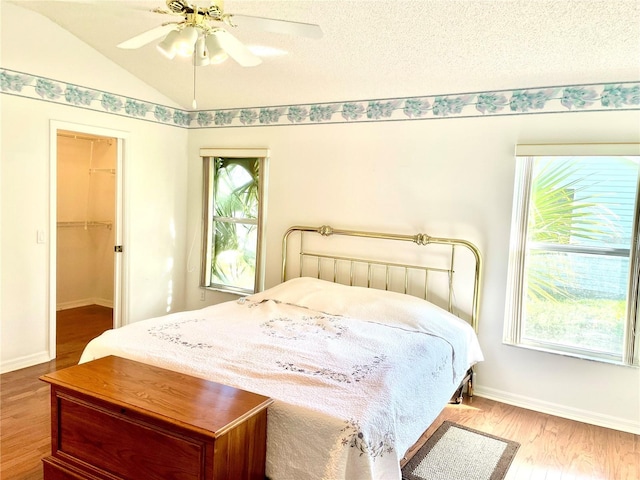 bedroom with a textured ceiling, baseboards, wood finished floors, a ceiling fan, and lofted ceiling