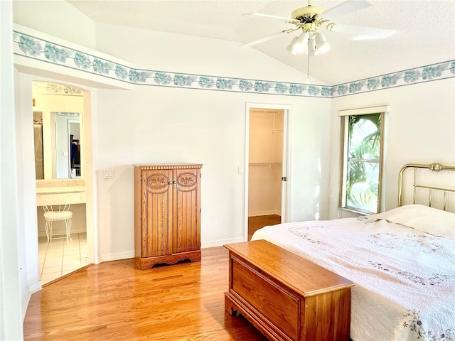 bedroom featuring baseboards, a ceiling fan, lofted ceiling, light wood-type flooring, and a walk in closet