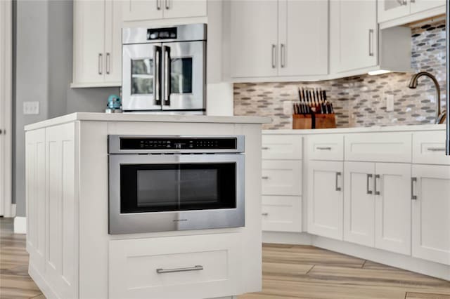 13112 Luntz Point Ln, Windermere, FL 34786 - kitchen featuring light wood-style floors, oven, decorative backsplash, and white cabinetry