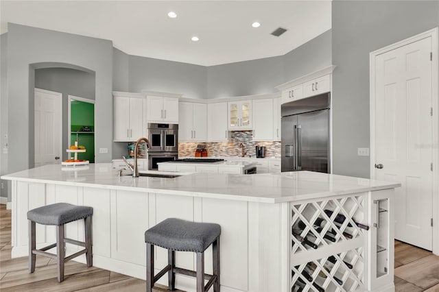 13112 Luntz Point Ln, Windermere, FL 34786 - kitchen with stainless steel appliances, a sink, light wood-style floors, white cabinetry, and arched walkways