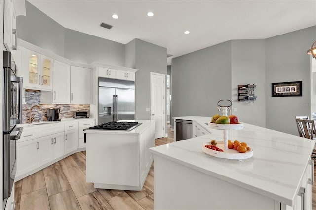 13112 Luntz Point Ln, Windermere, FL 34786 - kitchen with a kitchen island, appliances with stainless steel finishes, a sink, tasteful backsplash, and white cabinetry