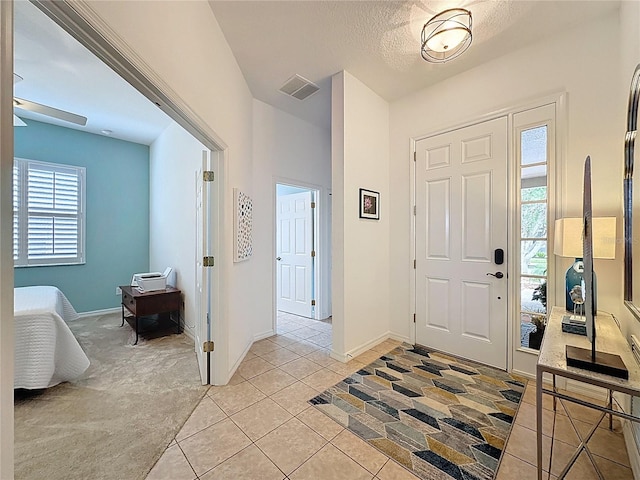 foyer entrance featuring baseboards, a textured ceiling, visible vents, and light tile patterned floors