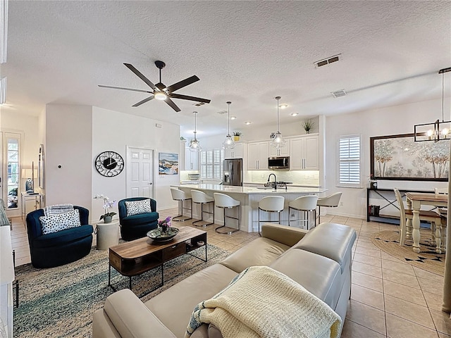 living area featuring light tile patterned flooring, ceiling fan with notable chandelier, and visible vents