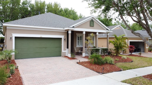 single story home with decorative driveway, an attached garage, roof with shingles, stucco siding, and covered porch