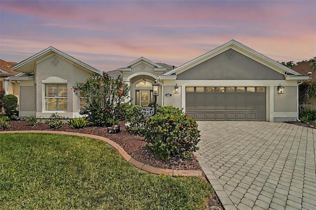 single story home featuring decorative driveway, a front yard, stucco siding, and a garage