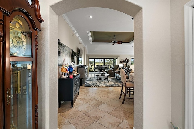 hall featuring a tray ceiling, arched walkways, ornamental molding, and light tile patterned floors