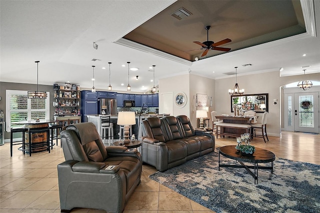 living area featuring a tray ceiling, light tile patterned floors, ceiling fan with notable chandelier, visible vents, and ornamental molding