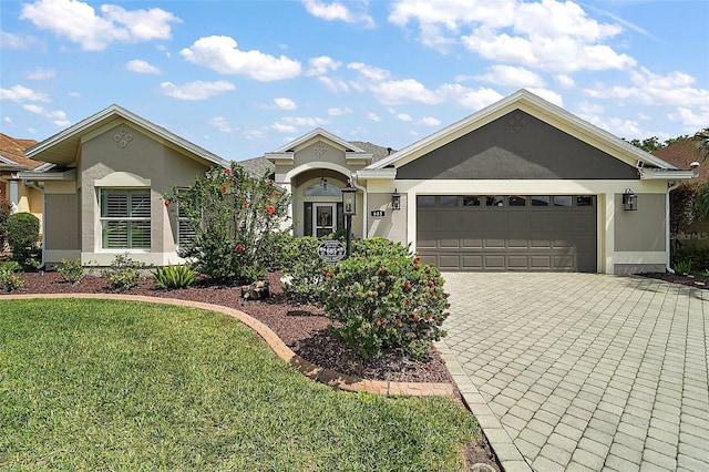 ranch-style home with a garage, a front yard, decorative driveway, and stucco siding