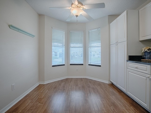 unfurnished dining area with baseboards, a textured ceiling, wood finished floors, and a ceiling fan