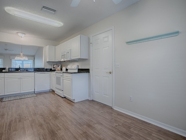 kitchen featuring white appliances, visible vents, dark countertops, and white cabinetry