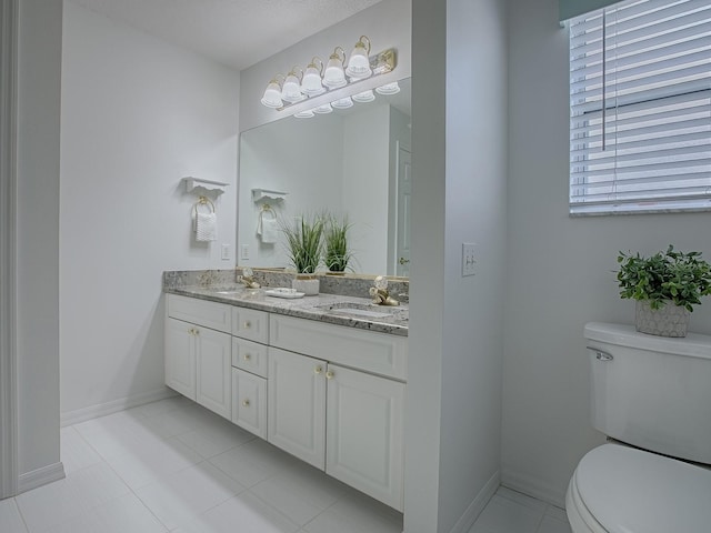 bathroom with baseboards, double vanity, a sink, and toilet