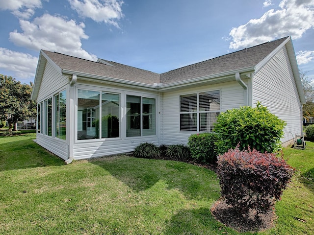 back of house with a lawn, a sunroom, and roof with shingles