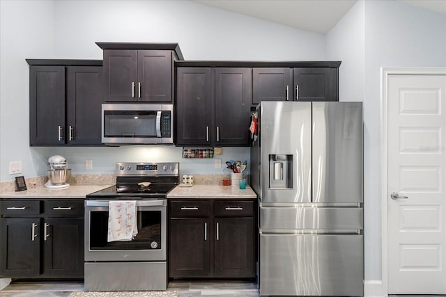 kitchen featuring vaulted ceiling, light stone countertops, dark brown cabinetry, and appliances with stainless steel finishes