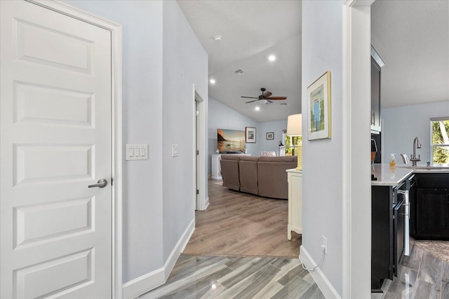 corridor with lofted ceiling, recessed lighting, baseboards, a sink, and light wood finished floors