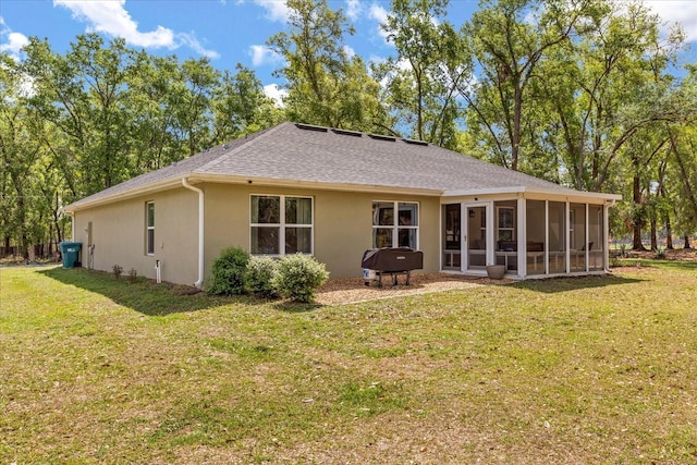 back of property with a sunroom, stucco siding, roof with shingles, and a lawn