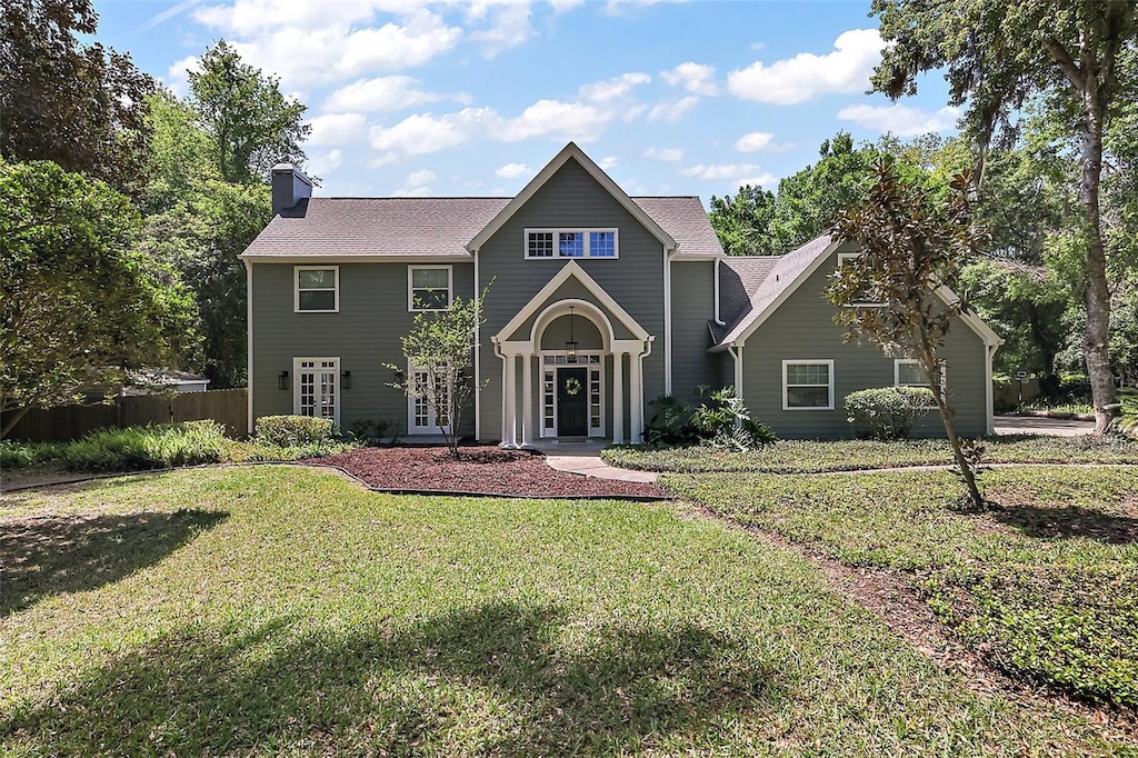 view of front facade featuring a front yard, french doors, fence, and a chimney